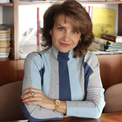 Smiling woman in a blue striped turtleneck sweater sitting in a bright home office setting.