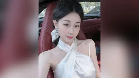 Elegant woman in a white satin halter dress and diamond earrings sitting in a luxury car interior.