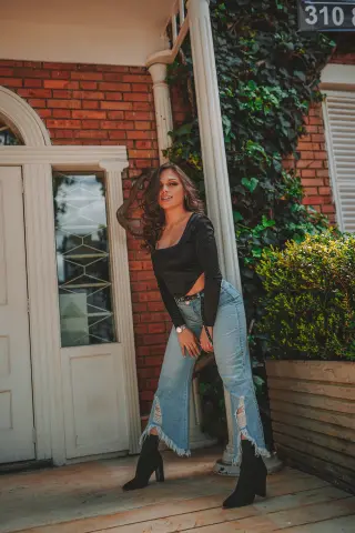 Stylish woman in a black long-sleeve crop top and light wash flared jeans posing by a brick house entrance.