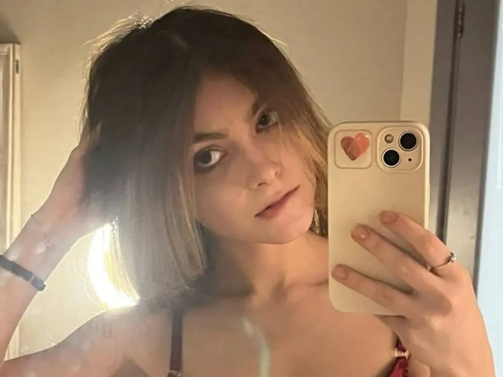 Young woman with blonde hair taking a moody mirror selfie in a dimly lit room.