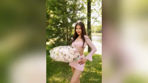 Smiling woman in a pink crop top and mini skirt holding a large bouquet of white roses in a sunny garden.
