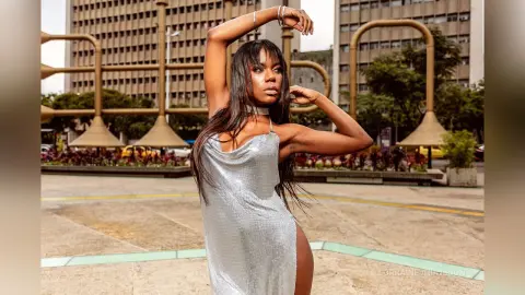 Stylish woman in a shimmering silver slip dress posing confidently in an urban city plaza.