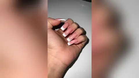 Close-up of long white French tip acrylic nails on a hand against a neutral background.