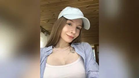 Smiling young woman in a white cap and blue shirt posing in a sunlit room.