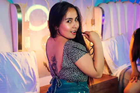 Smiling woman in leopard print top sitting in a neon-lit bedroom with a dreamy, moody atmosphere.