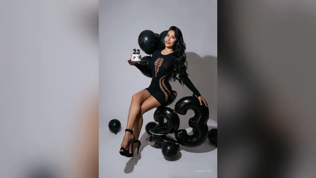 AnnMyer — Smiling woman in a black cocktail dress holding a 23 birthday sign with black balloons in a studio setting.