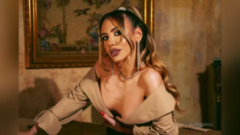 Glamorous woman in a beige off-the-shoulder outfit and silver jewelry posing in a vintage room.