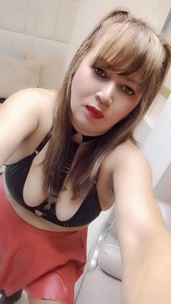 CharloteBrowns shows her bare chest and large breasts, wearing a black choker and a patterned top pulled down, with long brown hair and bangs.