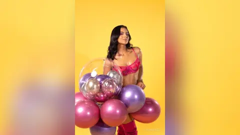 Glamorous woman in pink lingerie holding purple balloons against a bright yellow background.