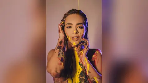 Artistic portrait of a woman with yellow paint dripping on her face and body in a moody studio setting.