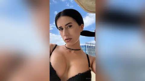 Young woman in a black lace bikini top posing under a sunny blue sky at an outdoor resort.