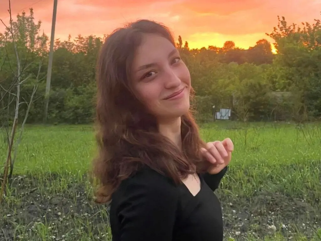 Smiling young woman in a black top enjoying a peaceful sunset in a lush green garden.