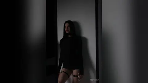 Moody portrait of a woman in a black long-sleeve outfit standing in a dark doorway.