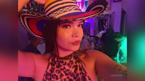 Young woman in a leopard print top and wide-brimmed hat posing in a vibrant, neon-lit nightclub setting.