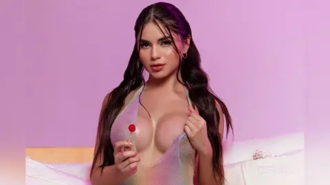 ValeryRouge wears a sheer mesh bodysuit while holding a red lollipop near her cleavage against a purple background.