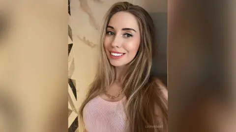 Smiling blonde woman in a pink ribbed tank top posing in a modern marble interior.