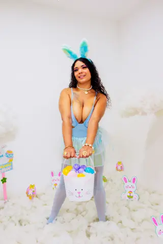Smiling woman in a blue bunny costume holding an Easter egg basket in a dreamy white cloud setting.