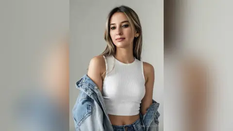 Young woman in a white ribbed crop top and denim jacket posing with a calm expression against a plain background.
