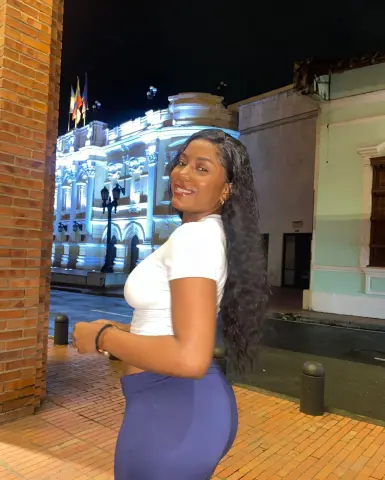 Smiling young woman in a white t-shirt and blue skirt posing at night in front of a lit classical building.