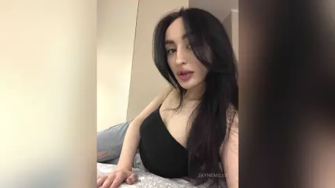 Young woman with long dark hair wearing a black tank top relaxing in a bright indoor setting.