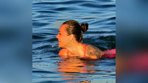 Smiling woman in a pink bikini swimming in the blue ocean water during a sunny summer day.