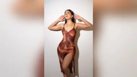 Elegant woman in a brown satin slip dress posing confidently against a white studio background.
