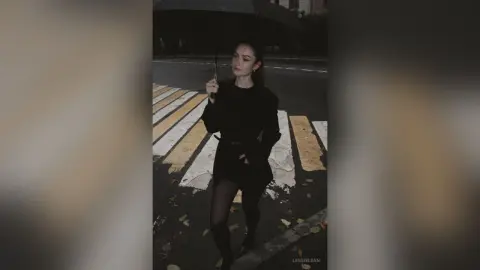 Moody portrait of a woman in an all-black outfit holding an umbrella on a city street at night.