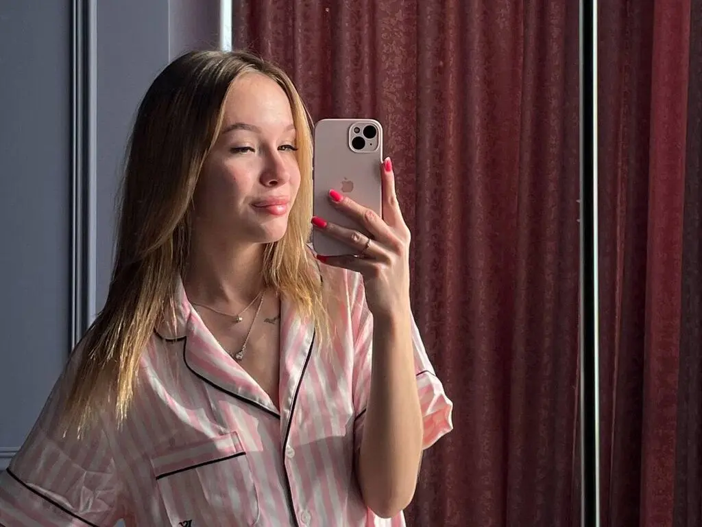 Young woman in pink striped pajamas taking a mirror selfie in a cozy bedroom setting.