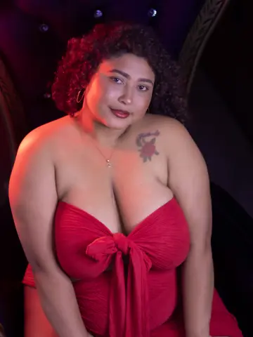 Curvy woman in a red strapless dress posing with a confident expression in moody, warm lighting.