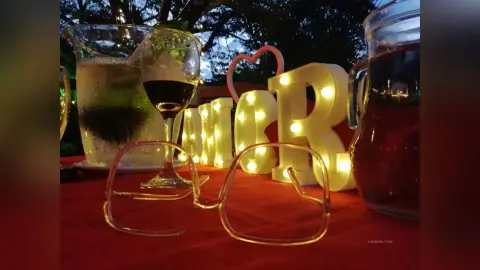 Romantic evening setting with red wine, glasses, and glowing heart decor on a red tablecloth at dusk.