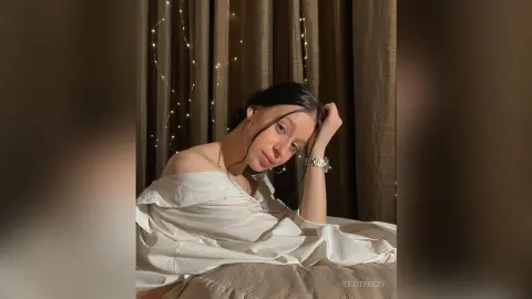 Young woman in a white off-the-shoulder blouse relaxing in a cozy room with warm fairy light decor.