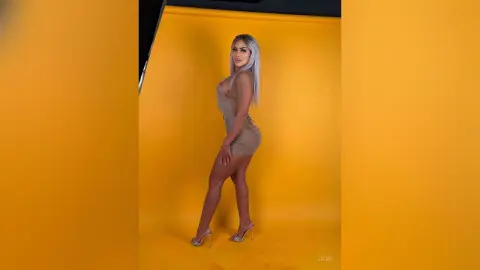 Glamorous woman in a sparkling gold mini dress posing against a vibrant yellow studio background.