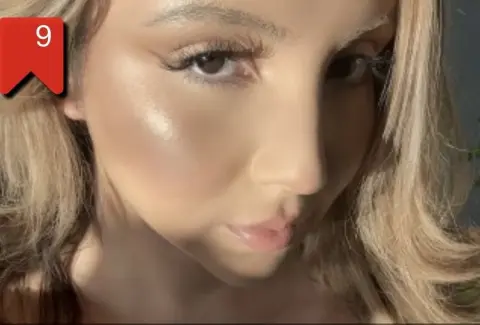 Close-up portrait of a blonde woman with glowing dewy makeup and soft natural lighting.