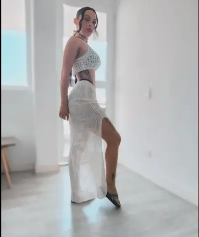 Woman in white crochet maxi dress and crop top posing in a bright, minimalist modern room.