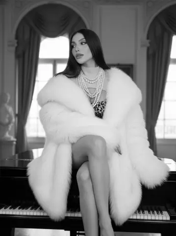 Elegant woman in white faux fur coat and pearl necklace sitting on a grand piano in a luxury classic room.
