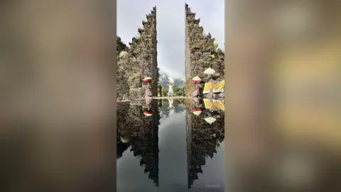 Serene traveler in white standing before the majestic stone gates of Lempuyang Temple in Bali reflected in water.