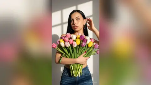 Young woman in denim holding a colorful tulip bouquet in bright, warm sunlight.