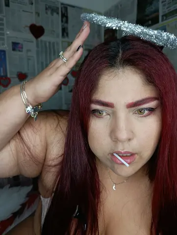 Woman with red hair and silver halo accessory posing in a room with heart wall decor.