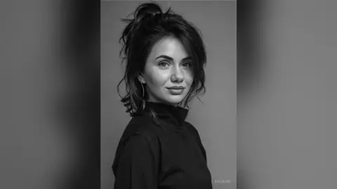 Portrait of a smiling young woman with messy bun hairstyle wearing a black turtleneck in a moody studio setting.