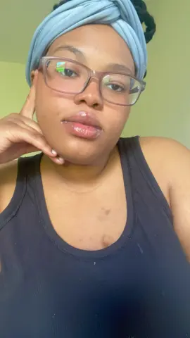 MilfArie22 wears a light blue headwrap and glasses, posing in a black tank top while resting her hand against her chin.