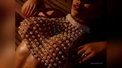 Glamorous woman in a beaded pearl mesh top posing in warm sunlight for a luxury fashion aesthetic.