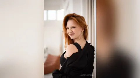 AlbertaCorrell is a redhead posing in a black top, looking over her shoulder with a playful smirk.