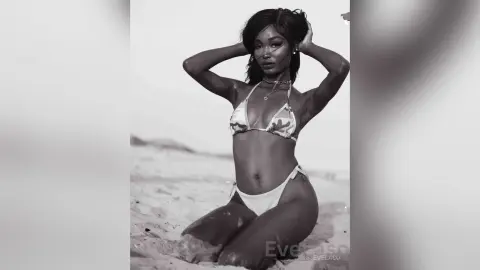 Confident Black woman in a patterned bikini posing on a sunny beach in a moody black and white portrait.