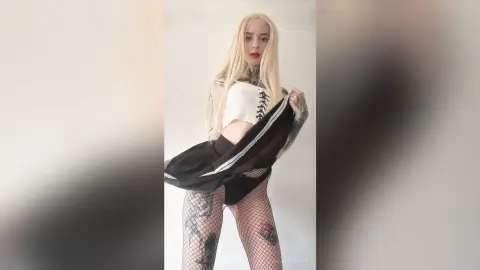 Blonde woman in a white crop top and black mini skirt posing in a minimalist indoor setting.
