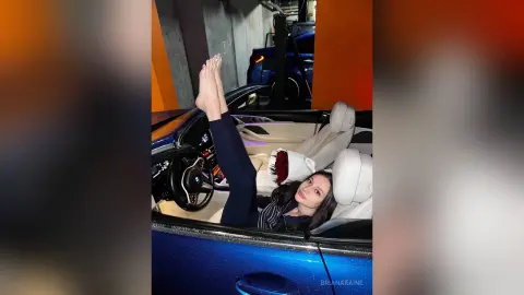 Young woman in dark clothing relaxing in a blue car interior with a playful and carefree mood.