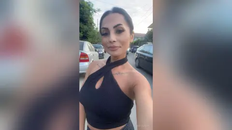 Smiling woman in a black halter top posing outdoors on a sunny street.