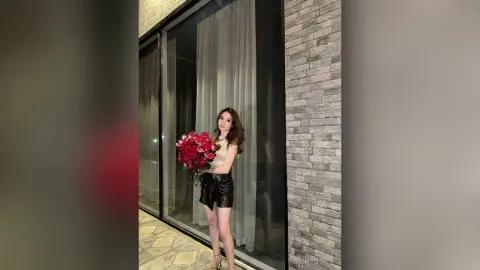 Elegant woman in a black leather skirt holding a large bouquet of red roses in a modern luxury interior.