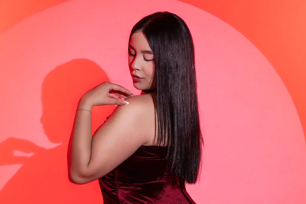 Young woman with long dark hair posing in a soft pink lit room with a dreamy mood.