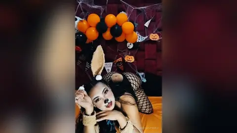 Woman in bunny ears and fishnet outfit celebrating a spooky Halloween party with orange balloon decor.