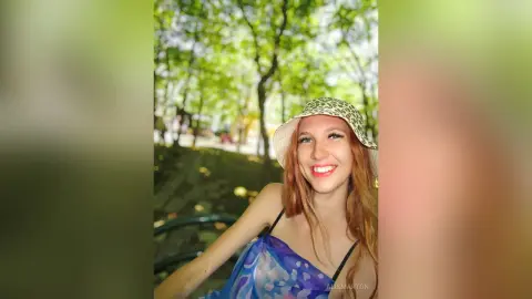 Smiling redhead woman in a blue floral summer dress relaxing in a sunny green park.